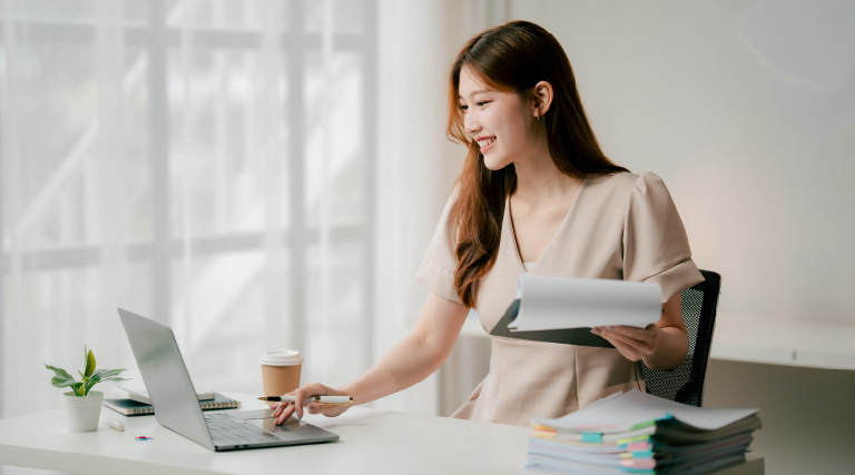 Young female adult learner with notes on left hand and scrolling laptop touchpad with right hand